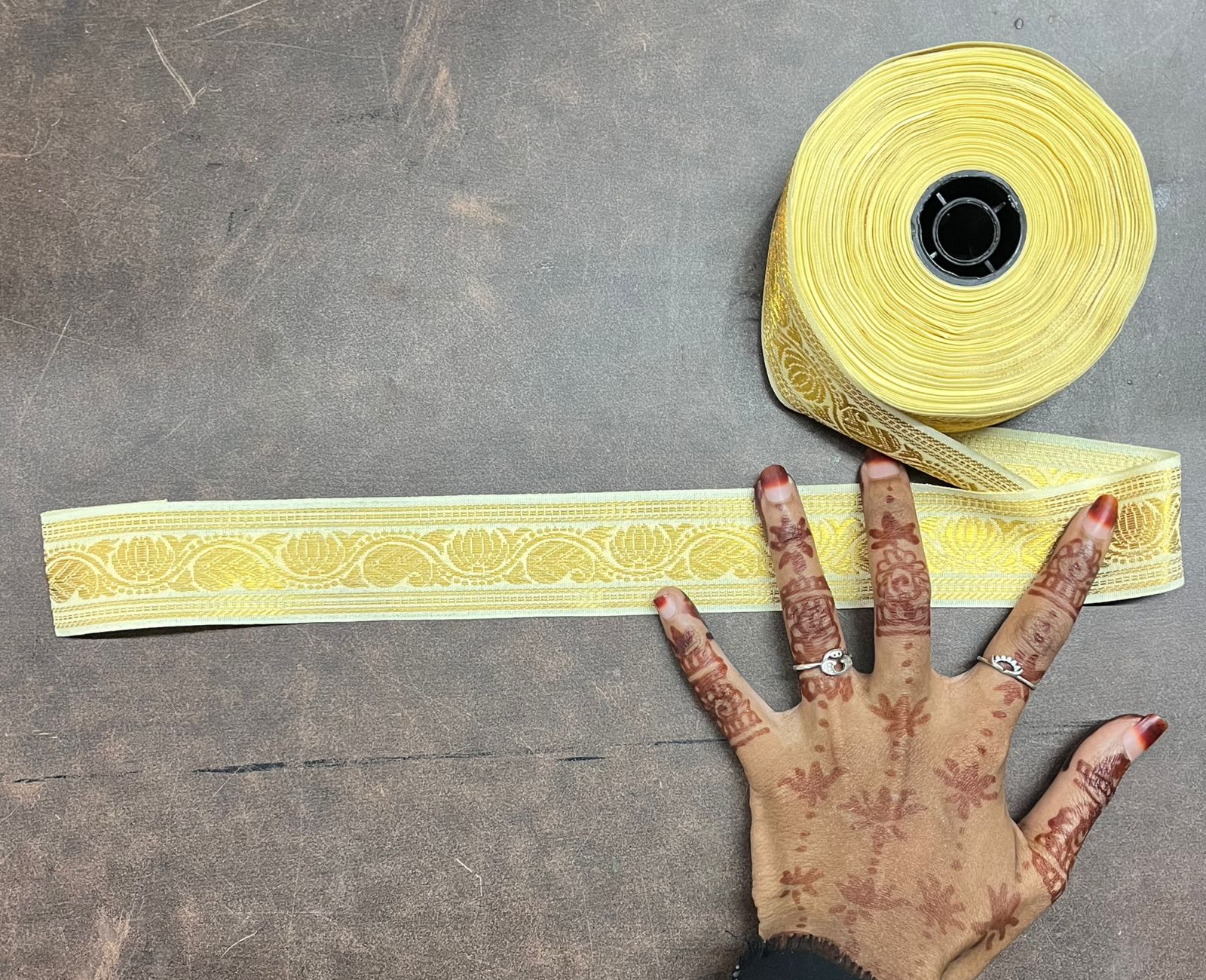 Roll of yellow decorative tape with a strip on a gray surface, next to a hand with henna designs.